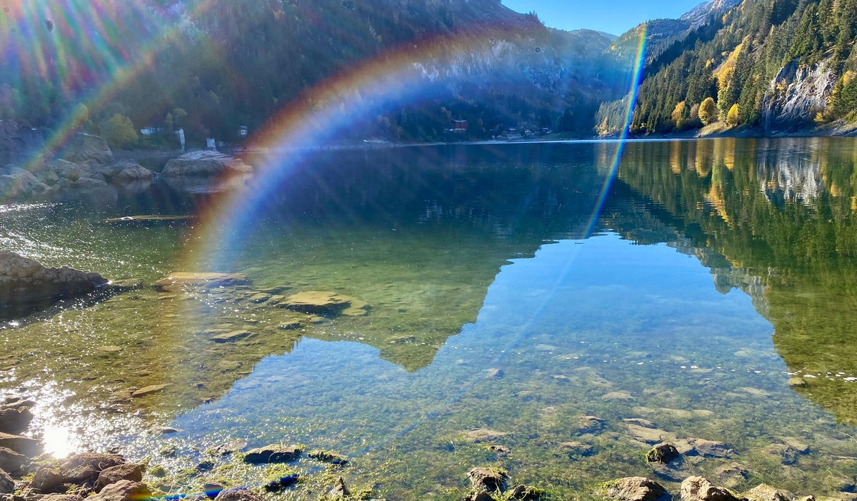 Un arc-en-ciel et son reflet sur un lac de montagne — le spectre des couleurs, chacune avec sa propre fréquence