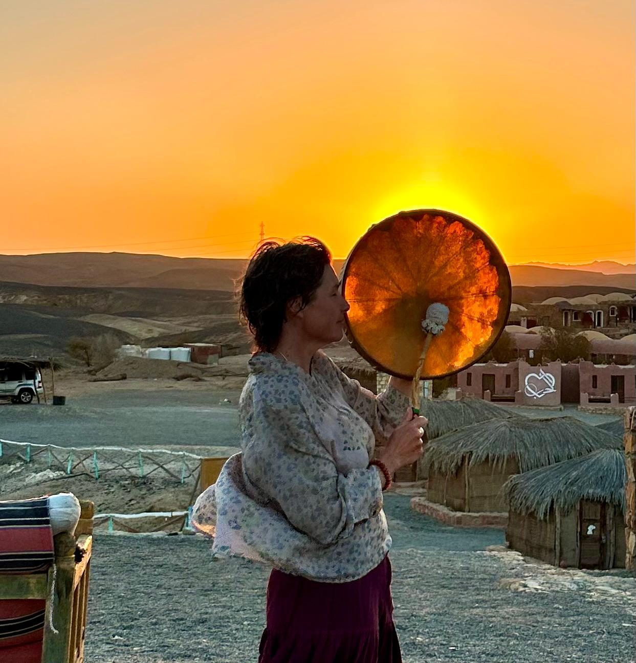 Nadiejda joue du tambour chamanique face au soleil couchant — la vibration qui relie le ciel et la terre